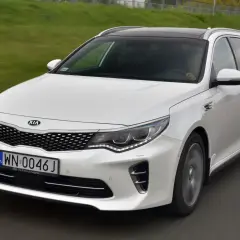 Biała Kia Optima w wersji kombi na drodze. Wiele osób szuka kia optima opinie przed zakupem.