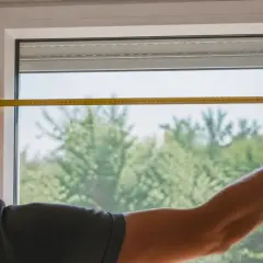 Un homme mesure une fenêtre avec un mètre ruban. Il est essentiel de savoir comment mesurer une fenêtre pour installer de nouveaux rideaux ou stores.