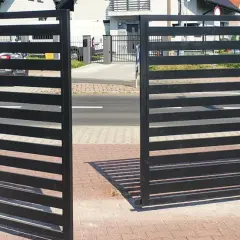 Nowoczesna, czarna brama otwierana na zewnątrz, z automatyką, stanowi eleganckie wejście na posesję.