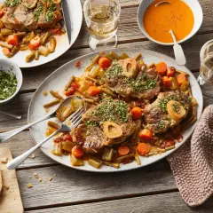 Ein festliches Mahl: saftiges Ossobuco mit Gemüse und einem Glas Weißwein. Dazu frisches Brot und eine cremige Tomatensuppe.