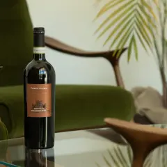 Bottiglia di vino rosso Poggio Miniera, un'eccellenza tra i vini toscani, su un tavolino di vetro, con poltrone verdi e piante sullo sfondo.