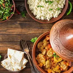 Stół z potrawami w stylu marokańskim: aromatyczny tagine z mięsem, kuskus, sałatka i chleb.