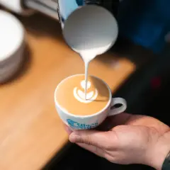 Barista tworzy latte art na flat white. Mleczna pianka układa się w kształt kwiatu na kawie.