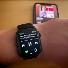 Apple Watch zeigt Spotify-Song "Everything Went Numb" von Streetlight Manifesto. Ein iPhone im Hintergrund spielt ebenfalls Musik.