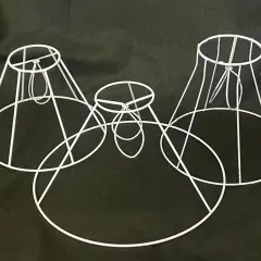 Estructuras de **lámpara alambre** blancas, de diferentes tamaños, dispuestas sobre fondo oscuro.