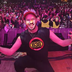 Max Pezzali sul palco, con la folla illuminata dai cellulari, indossa una maglietta con il logo 883.