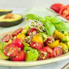 Frischer **avocado tomaten salat** mit Basilikum und Sprossen, garniert mit roten und gelben Kirschtomaten.