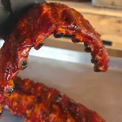 En hand i svart handske håller upp saftiga, grillade revben. De glänser av glaze och ser otroligt goda ut.