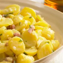 Ein cremiger Kartoffelsalat mit Speck und Petersilie, serviert in einer hellen Schüssel.
