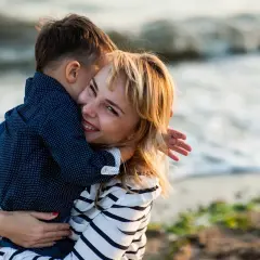 Uśmiechnięta kobieta mocno przytula chłopca na plaży. To idealny dzień cioci, pełen miłości i radości.