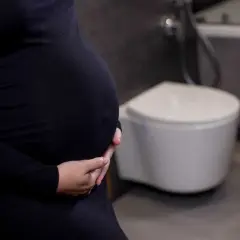 Gravid kvinna med händer på magen, toalett i bakgrunden. Vanliga besvär som uvi kan drabba gravida.
