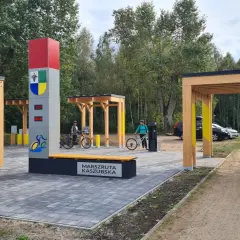 Nowiutka stacja rowerowa na Marszrucie Kaszubskiej. Dwie panie z rowerami, nowoczesna infrastruktura i leśne otoczenie.