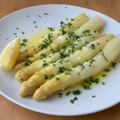 Välkokt vit sparris serverad på en vit tallrik med smält smör, hackad persilja och en citronklyfta. Enkel och god rätt!