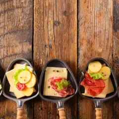 Petites coupelles pour un apéritif raclette, garnies de fromage, charcuterie et pommes de terre sur fond de bois.