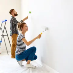 Coppia felice imbianca casa con rullo, trasformando le pareti bianche in un nuovo inizio.