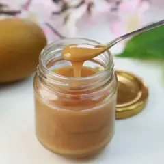 Gęsty, złocisty miód manuka na łyżeczce, obok owoców kiwi. Odkryj niezwykłe miód manuka właściwości.