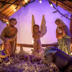 Portal de Belén manualidades: figuras de San José, la Virgen María, un ángel, el Niño Jesús, un buey y una mula, iluminados con luces navideñas.