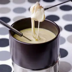 Un morceau de pain trempé dans une fondue au comté crémeuse, filant sur une fourchette.