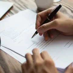 Ręka pisze na dokumentach. Jeśli masz problem z adwokatem, dowiedz się, gdzie można złożyć skargę.