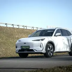 Biały Geely EX5 na tle słonecznego nieba i zielonych wzgórz. Elegancki SUV gotowy na podróż.