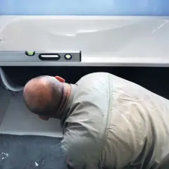 Un homme vérifie le niveau d'une baignoire avant de la fixer. L'outil de mesure est posé sur le rebord.
