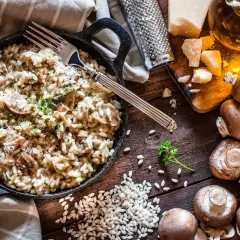 Un cremoso risotto de setas servido en sartén de hierro fundido, con champiñones frescos, arroz, queso parmesano y perejil picado.