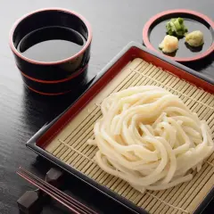 Prosty makaron udon przepis: grube kluski na bambusowej macie, miseczka z sosem i dodatkami. Idealne danie.