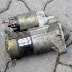 Dwa zużyte rozruszniki w aucie leżą na chodniku. Jeden ma naklejkę z napisem "MITSUBISHI JAPON".