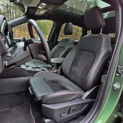 Wnętrze Ford Kuga z czarną tapicerką i czerwonymi przeszyciami. Widok na fotel kierowcy, deskę rozdzielczą i fragment dachu panoramicznego.