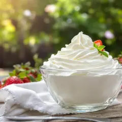 Un bol de crème chantilly qui tient longtemps, garni d'une fraise et d'une feuille de menthe, entouré de fraises fraîches.