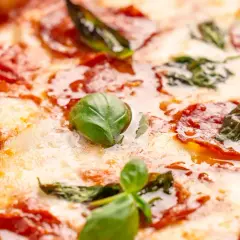Nahaufnahme einer Pizza mit geschmolzenem Käse, roten Salami-Scheiben und frischem Basilikum. Verschiedene Salami-Sorten machen diese Pizza unwiderstehlich.