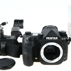 Czarny aparat Pentax K-3 III, ładowarka i akcesoria. Czy to lustrzanka czy bezlusterkowiec? To lustrzanka.