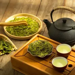 Zaparzanie sencha green tea. Suszone liście, czajniczek i dwie filiżanki z naparem na drewnianej tacce.
