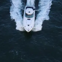 Un bianco yacht naviga veloce, lasciando una scia di spuma. La sua posizione è centrale, in un mare scuro e mosso.
