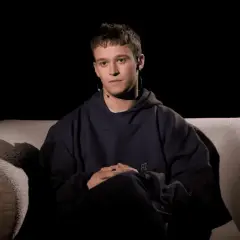 Xavier Michał Wiśniewski, młody mężczyzna w granatowej bluzie z kapturem, siedzi na kanapie, zamyślony.