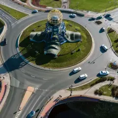 Widok z lotu ptaka na ronda turbinowe i jak jeździć. Samochody i autobus poruszają się po skomplikowanym skrzyżowaniu z centralną rzeźbą.