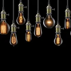 Rząd wiszących lamp w kształcie żarówki, każda z unikalnym, ozdobnym żarnikiem i mosiężnym mocowaniem, tworzy ciepłą, nostalgiczną atmosferę.
