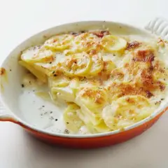 Patatas gratinadas con queso cremoso y dorado, recién salidas del horno en una cazuela naranja.