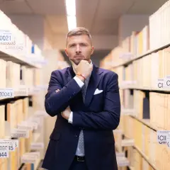 Mężczyzna w garniturze zastanawia się, jak liczyć 6 miesięcy na odrzucenie spadku, wśród regałów pełnych akt.