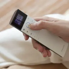 Mano ajustando el aire acondicionado a 21 grados. El mando muestra el modo "cool" para un ambiente fresco.
