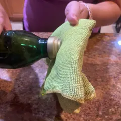 A hand pours olive oil from a green bottle onto a green microfiber cloth, suggesting it's the best home remedy to clean stainless steel.