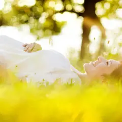 Une femme enceinte, baignée par le soleil, sourit en se prélassant dans l'herbe verte.