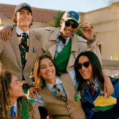 Grupo de jóvenes sonriendo, vestidos con estilo preppy: trajes, corbatas, chalecos y gorras.