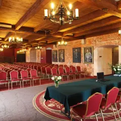 Elegancka sala konferencyjna w hotelu z **luxury collection**, z rzędami czerwonych krzeseł, drewnianym sufitem i ceglanymi ścianami.