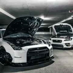 Deux voitures de sport blanches, capots ouverts, révélant leurs moteurs. Ces chevaux fiscaux, prêts à rugir, sont garés dans un parking sombre.