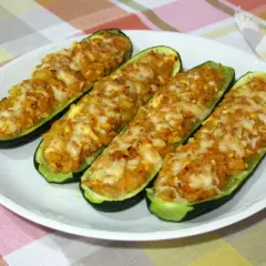 Cuatro calabacines rellenos de atún, gratinados con queso, servidos en un plato blanco sobre un mantel a cuadros.