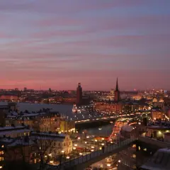 Stockholms silhuett i skymningen, med upplysta byggnader och en bro. Tänk dig en mosebacke konsert här.