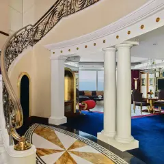 Luksusowe wnętrze z marmurowymi schodami, złotymi zdobieniami i niebieskim dywanem. To widok, który może towarzyszyć pobytowi w Burj Al Arab, gdzie burj al arab cena za noc odzwierciedla tę elegancję.