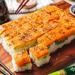 Low-Carb-Sushi mit Lachs und Avocado, bestreut mit Sesam, auf einem Holzbrett.