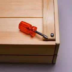 Cacciavite arancione su un mobile in legno grezzo, pronto per essere restaurato.